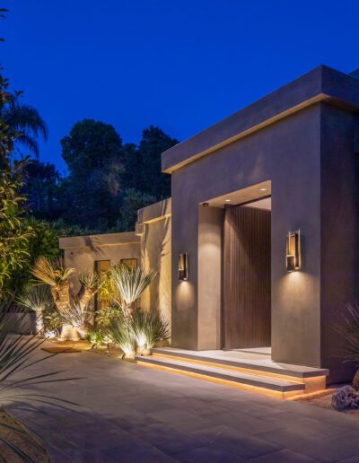 Illuminated modern home entrance with landscaped pathway at dusk.