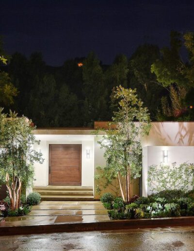 Modern house exterior illuminated at night with landscaped driveway and garage.