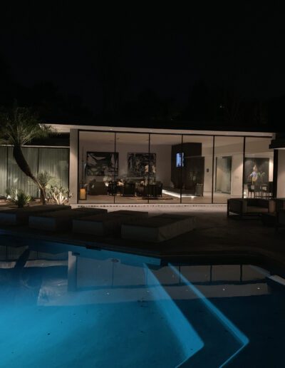 A modern house at night with interior lights on and an illuminated swimming pool in the foreground.