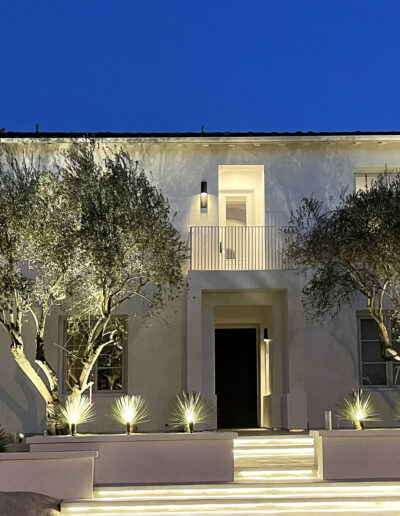 Modern two-story house with exterior lighting and landscaped front yard at dusk.